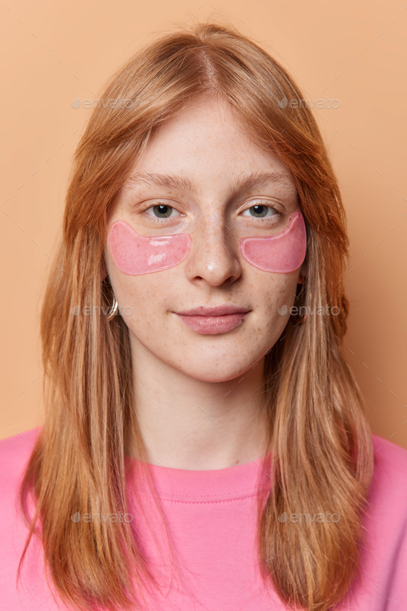 Vertical shot of serious pretty redhead girl applies hydrogel patches under eyes reduces bags looks