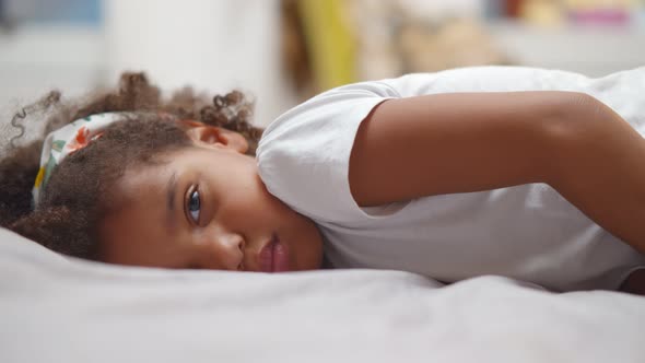 Little Cute African American Girl Lying on Bed and Smiling at Camera alt