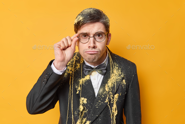 Horizontal shot of attentive serious man keeps hand on rim of spectacles dressed in festive suit sme