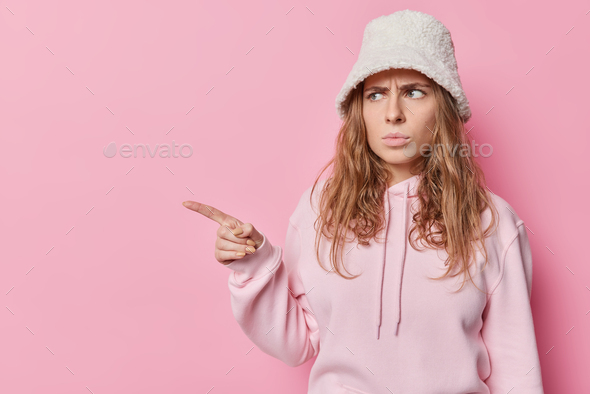 Moody dissatisfied young woman frowns face points idex finger away makes upset discontent grimace fr