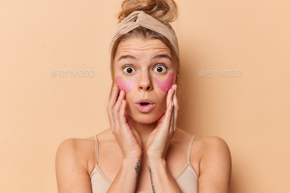 Shocked Fair Haired Young Woman Keeps Hands On Cheeks Stares Bugged