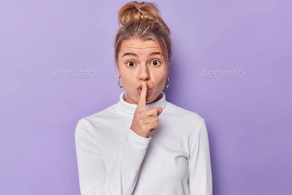 Please tell nobody. Surprised young lovely woman makes silence gesture says shh asks do not speak or