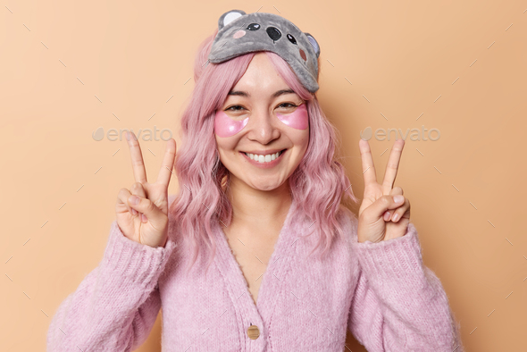 Cheerful young Asian woman with dyed pink hair applies hydrogel patches under eyes to remove wrinkle