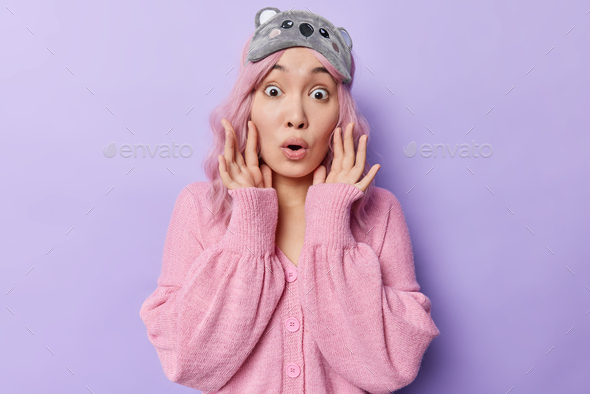 Stupefied Asian woman with pink dyed hair reacts on something impressive holds breath stands wondere