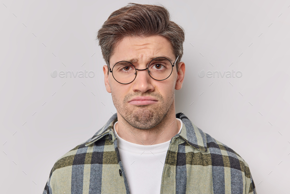 Portrait of sad unhappy man frowns face upset with bad news he received wears round spectacles and c