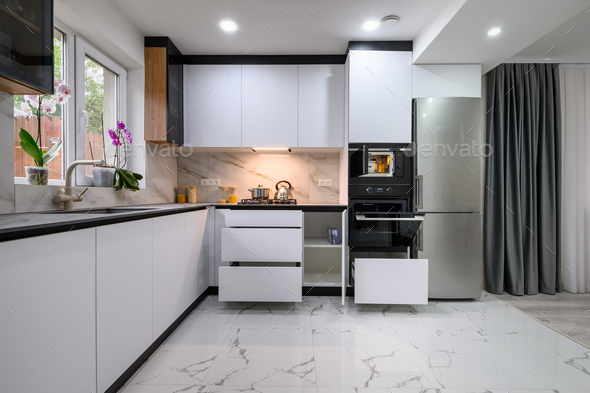 A functional and stylish kitchen with a white design, a marble floor, an open oven door, and pull