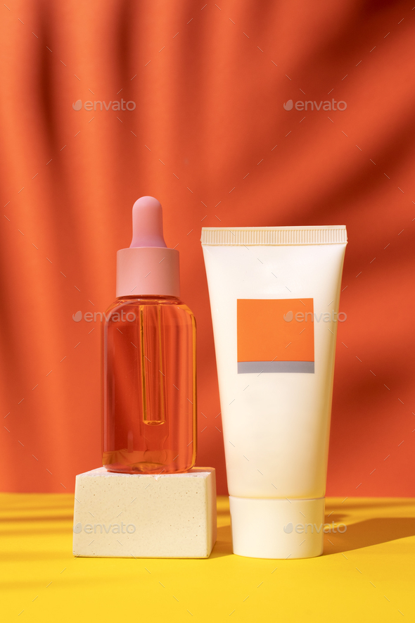 Cosmetic bottle with oil and tube with cream on podium on orange background with palm leaves shadow