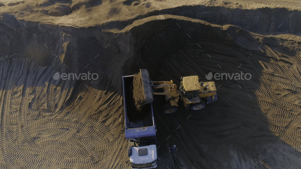 Top view of excavator with dump truck at quarry. Scene. Excavator fills dump truck at quarry with