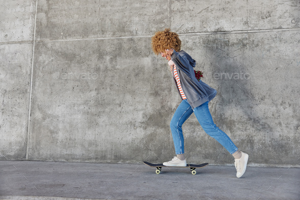 Energetic hipster girl rides skateboard dressed in casual clothes