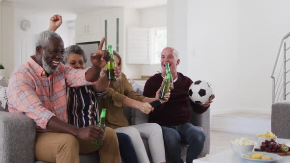 Two diverse senior couples sitting on a couch watching a game drinking beer cheering alt