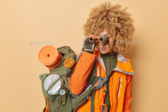 Female explorer looks in binocular explores new places carries big rucksack with necessary things fo
