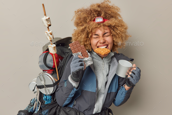 Photo of positive female explorer eats waffles sweet chocolate and drinks tea from mug dressed in ac
