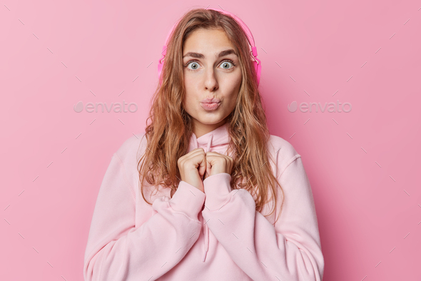 Photo of surprised blue eyed woman keeps hands together has lips rounded long dark hair dressed in c