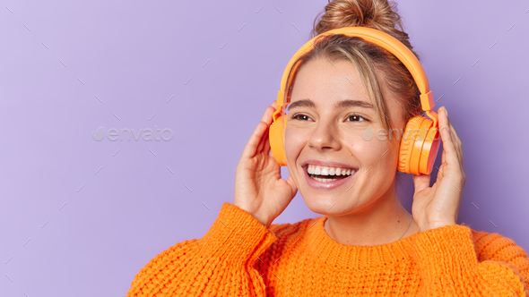 Close up shot of young positive woman listens music in wireless headphones  feels free poses in cente Stock Photo by wayhomestudioo