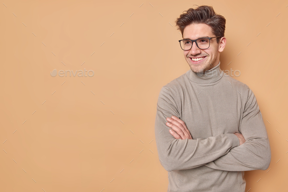 Positive self confident man keeps arms folded looks away with satisfied expression listens good news