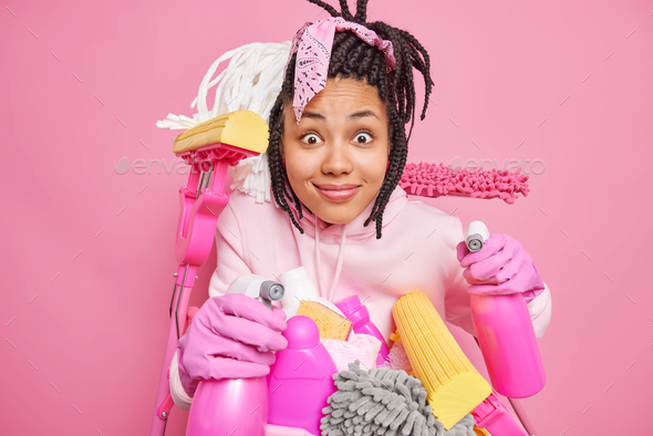 Surprised young woman housekeeper does chores cleans house uses cleaning detergents and equipment ti