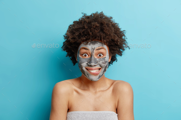 Surprised Curly Haired Woman Bites Lips Looks Wondered At Camera