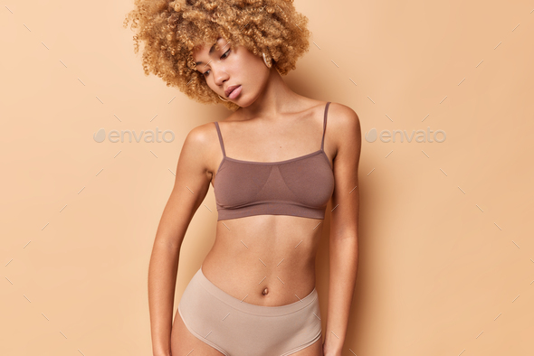 Studio shot of thoughtful curly haired woman concentrated down