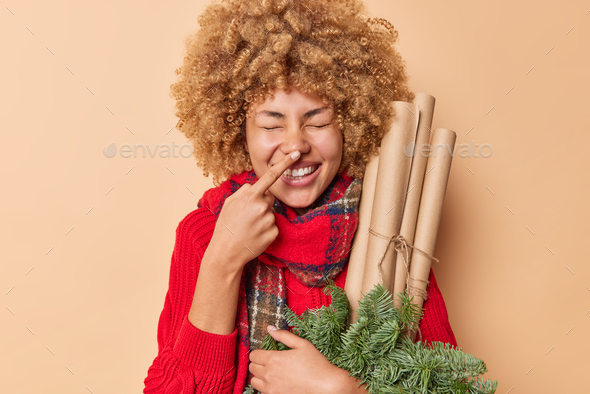 Positive playful woman with curly bushy hair touches nose foolishes around works as florist prepares