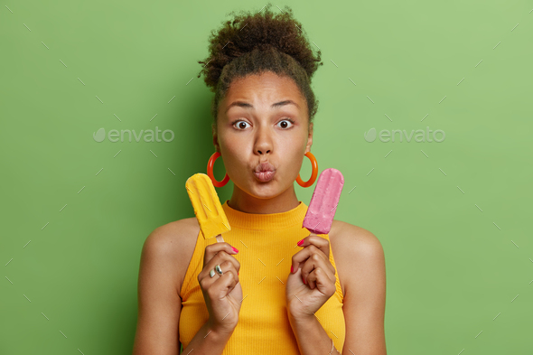 Temptation and chilling concept. Surprised curly haired youngwoman holds two appetizing ice creams k