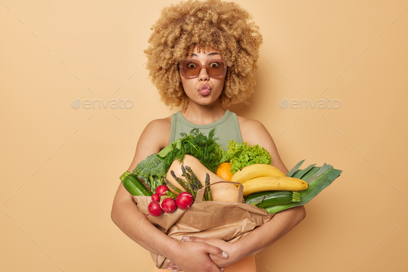 Spring harvest. Curly haired young woman keeps lips folded embraces bouquet with fresh picked vegeta