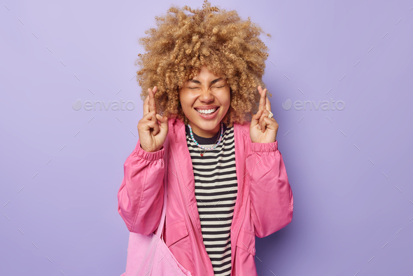 Cheerful woman keeps fingers crossed puts all efforts in wishing good luck believes in dreams come t