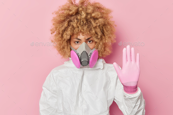 Serious woman chemist shows stop gesture wearsprotective suit ...