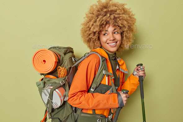 Positive active female hiker poses with scandinavian sticks tries to reach top of mountain dressed i
