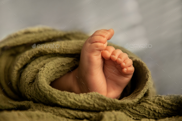 Closeup of newborn baby feet in a green wrap at natural light, indoor photography - Stock Photo - Images