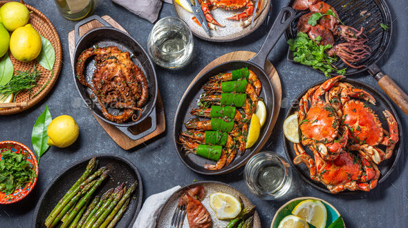 Set table with seafood dishes - cooked crabs, tiger shrimps, grilled octopus and squids on cast iron