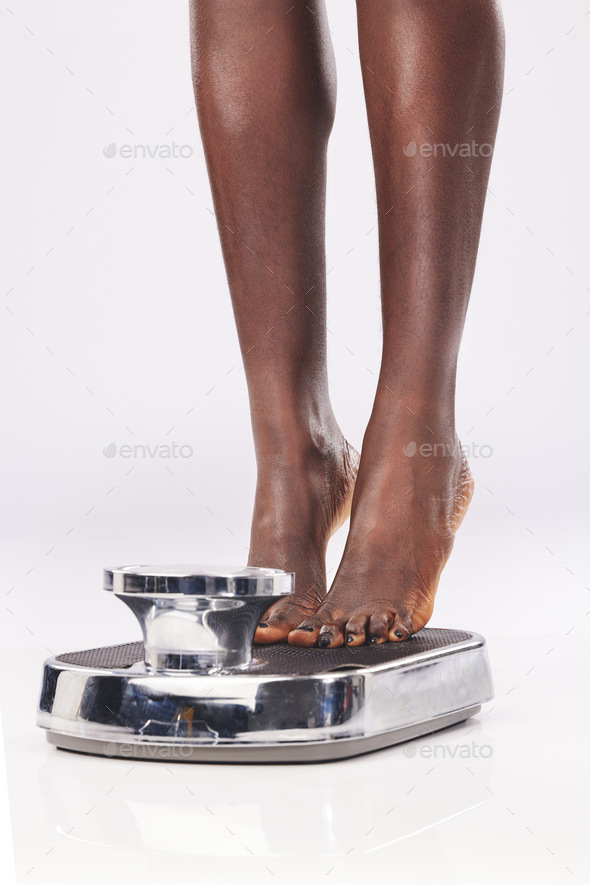 Black woman, feet and scale to measure weight, diet and weightloss against a white studio back with