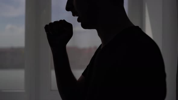 Silhouette of a Coughing Man on a Window Background. The Patient Is Treated at Home for the Virus alt