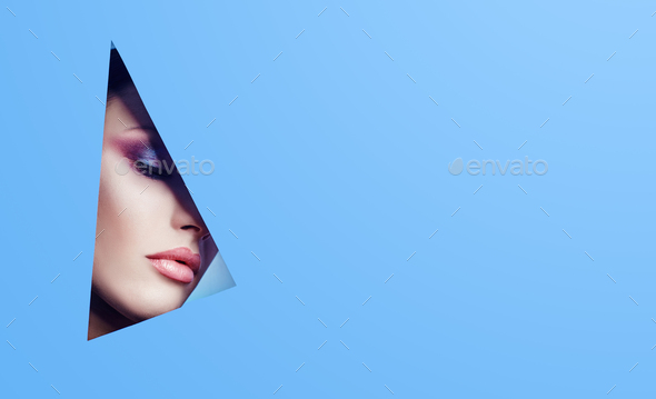 Woman with a beautiful look through a triangular hole in the blue paper, bright makeup