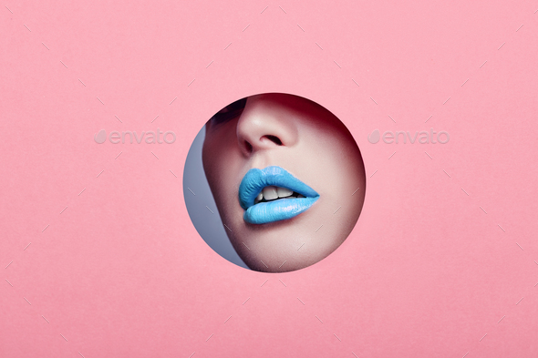 Advertising Beautiful plump lips bright blue color, woman looks in hole colored pink paper