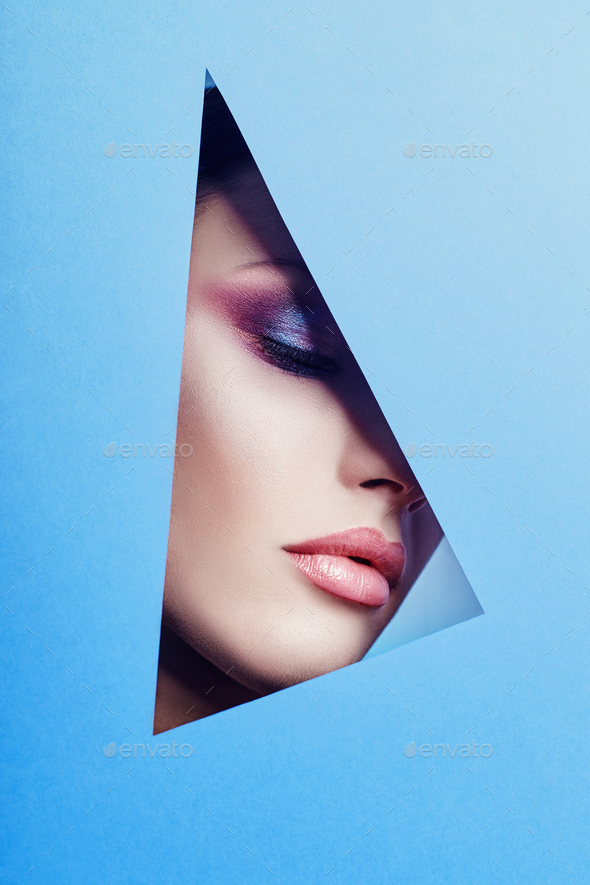Woman with a beautiful bright makeup and pink lipstick looks through a triangular hole