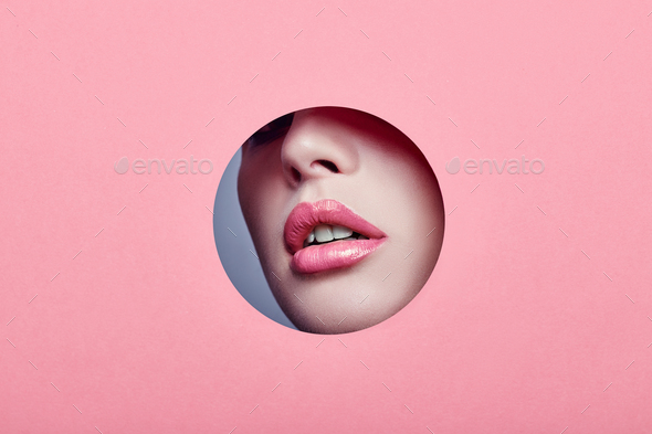 Advertising Beautiful plump lips bright pink color, woman looks in hole colored pink