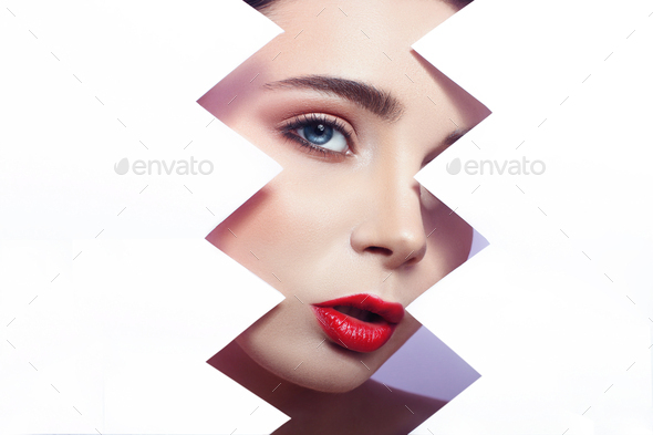 Woman looks into the hole of torn paper, bright beautiful makeup, big eyes and lips
