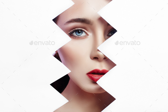 Woman looks into the hole of torn paper, bright beautiful makeup, big eyes and lips