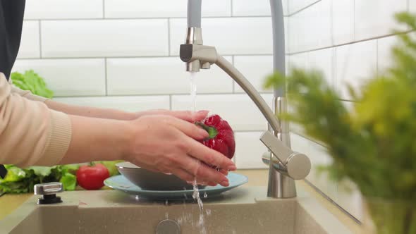 Closeup of a Young Girl Washing Red Bell Peppers at Home in the Kitchen alt
