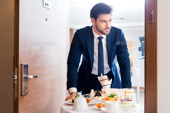 selective focus of handsome receptionist bringing breakfast on hotel food trolley
