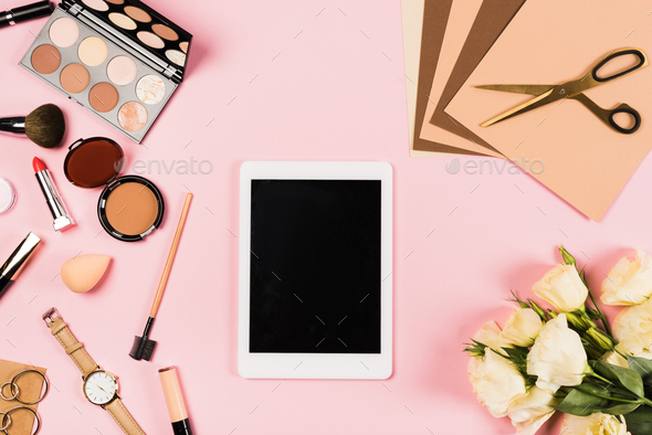 top view of digital tablet with blank screen, flowers and decorative cosmetic on pink