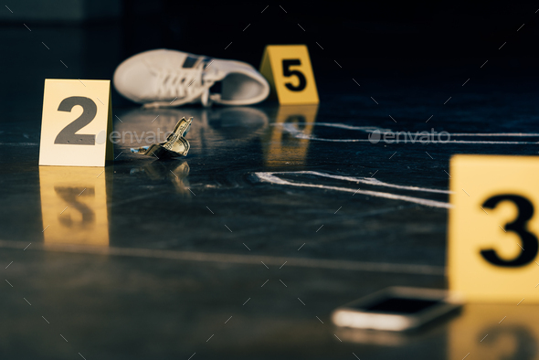 selective focus of smartphone, chalk outline, shoe, dollar banknote and evidence markers at crime