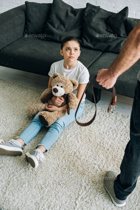 overhead view of abusive father holding belt and scared daughter with ...