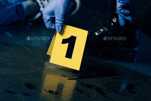 partial view of investigator in rubber gloves with evidence marker at crime scene