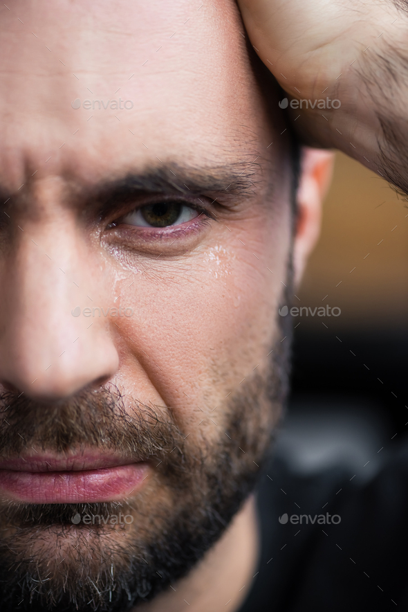 partial view of depressed bearded man crying and looking at camera