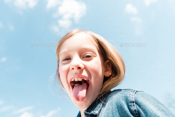 low angle view of happy kid showing tongue under sky