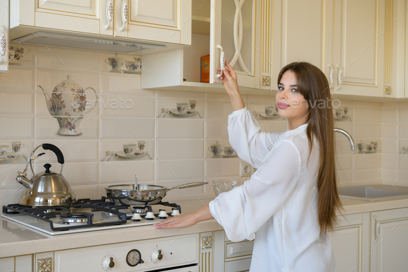 A beautiful young woman is opening a kitchen cabinet