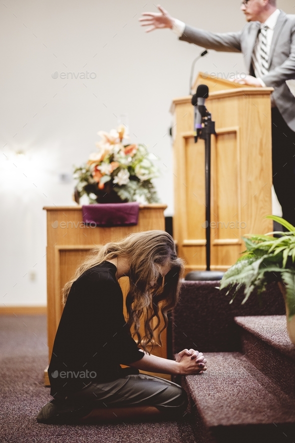 Woman at the front of a church kneeling down and praying