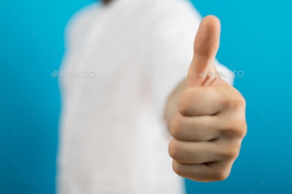 Closeup of a person doing the thumbs-up gesture under the lights on a blurry background