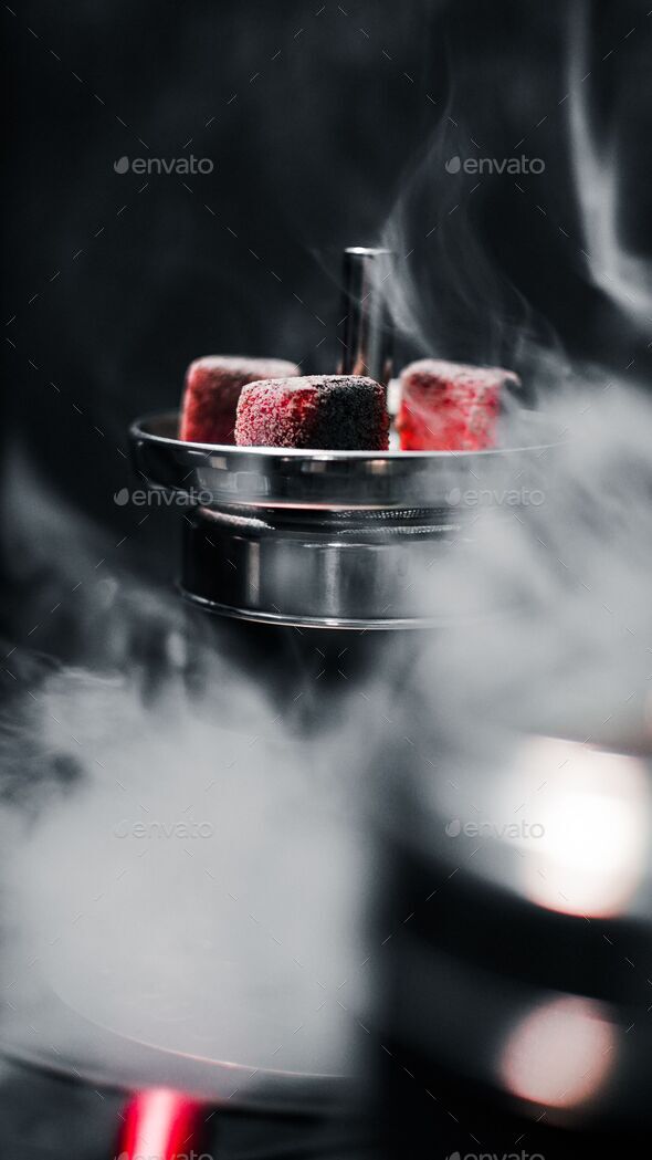 Vertical shot of bright red charcoal cubes on metal shisha in dark smoky gaming room